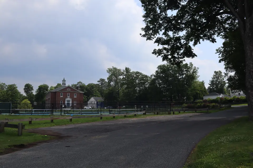 Gravel parking lot in the back of community center, providing parking for at least 14 cars.