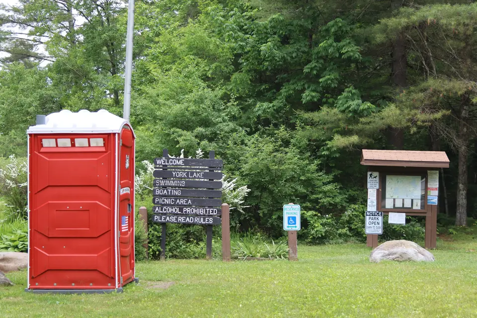 A portable restroom and an accessible parking space at the front of the parking area.