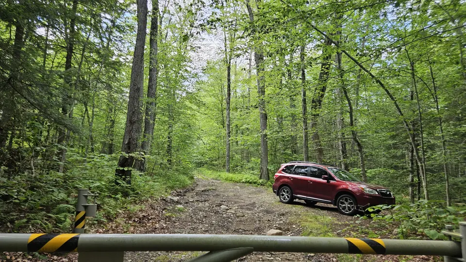 The trailhead, seen from the trail. With a gate at the entrance and a car in the parking area.