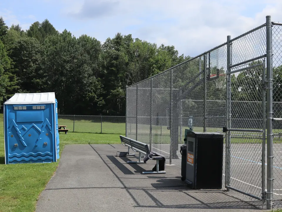 A paved path allows access to a portable restroom and the basketball court.