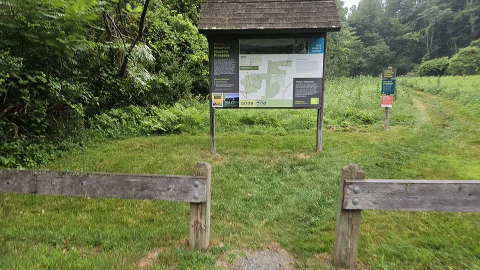 A 4-foot gap between a fence at the trailhead. A sign for the trail seen behind the fence.
