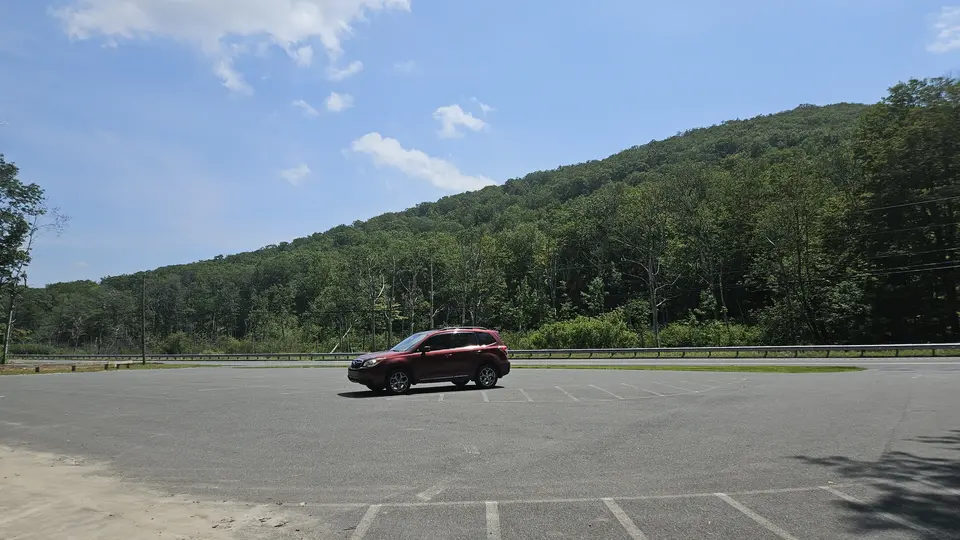 The paved parking lot, with green mountains in the background.
