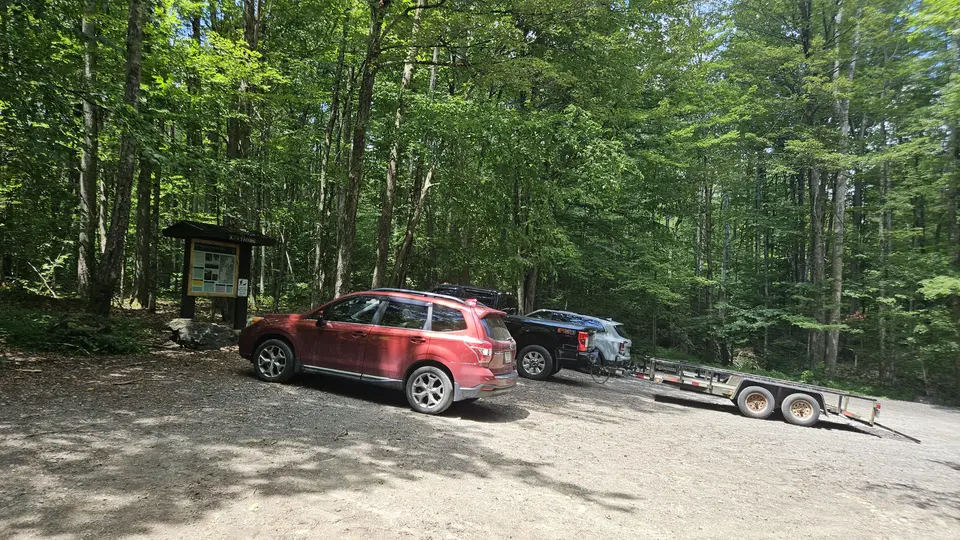 Cars in a gravel parking lot near a trailhead sign.