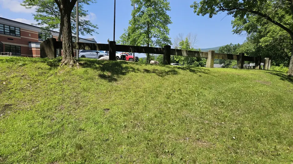 A grass slope that leads down to the trailhead. Adjacent to a set of stairs.