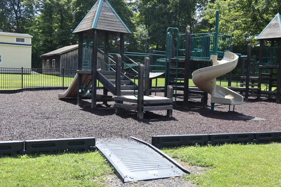 A short ramp provides an accessible route into the enclosed playground. The playground material is crushed tire.